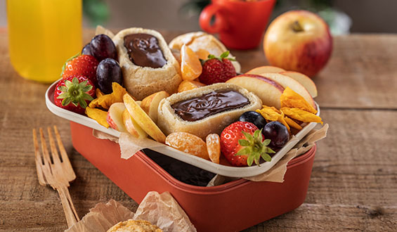 A kids lunchbox full of fruit and white penny loaf filled with chocolate spread