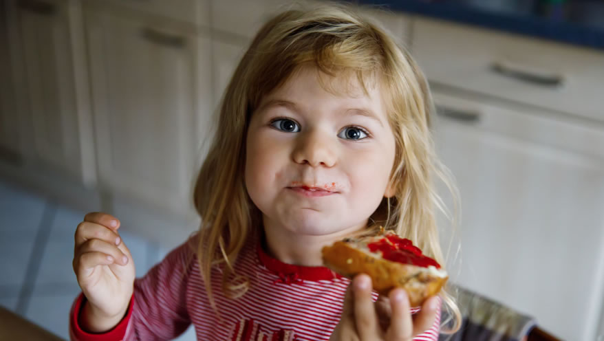 A little girl eating bread with jam on top